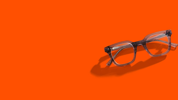 Hymyilevä silmälasipäinen nainen oranssia taustaa vasten